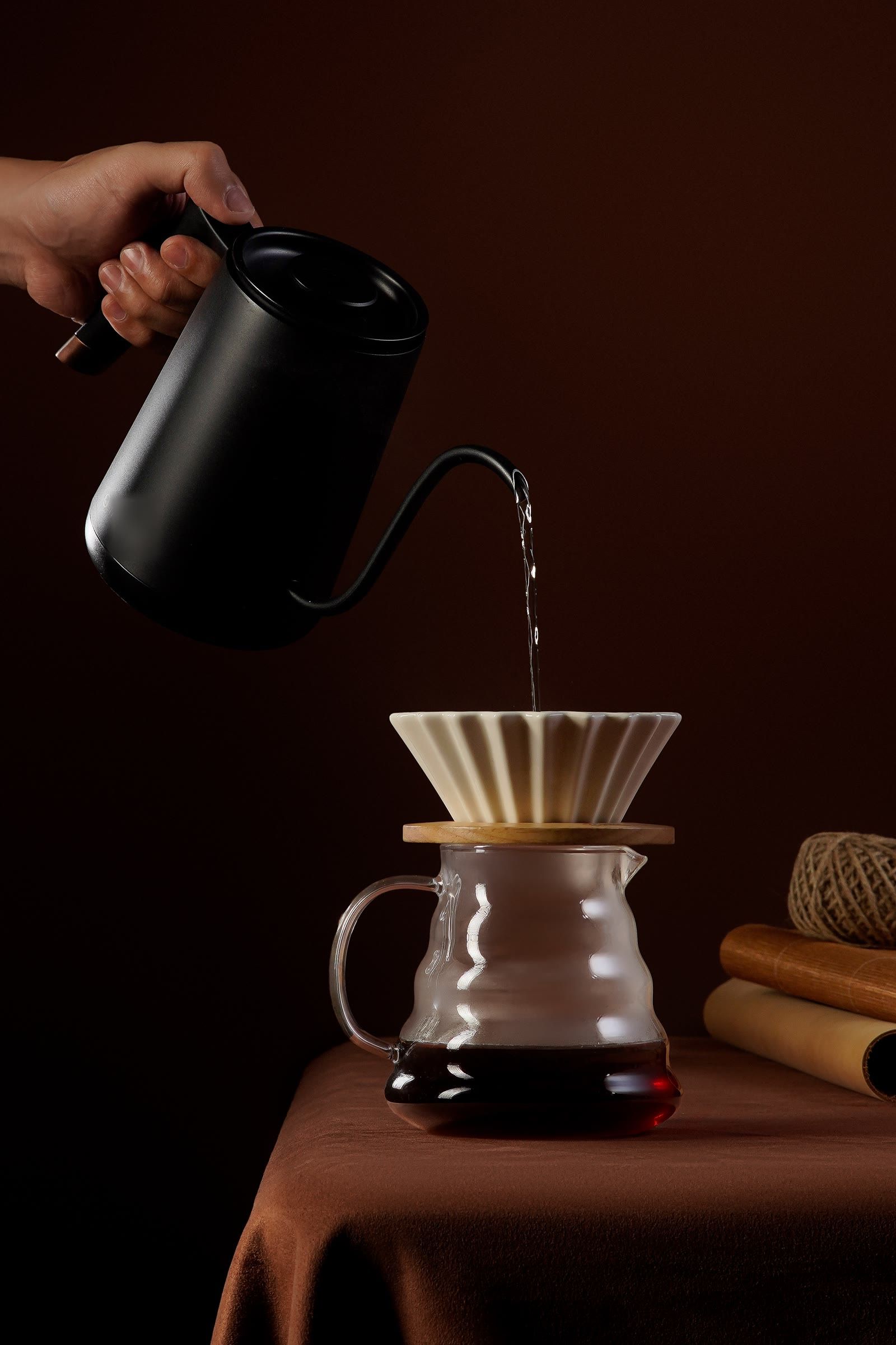 A hand pours water from a gooseneck kettle over a ceramic dripper, steam rising.